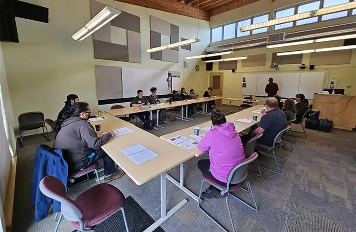 People seated around U-shaped tables in a meeting room, reviewing documents.