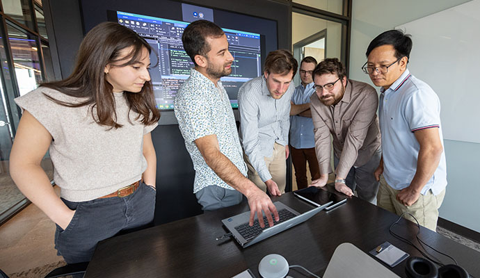 Group of researchers stand over laptop looking at data.