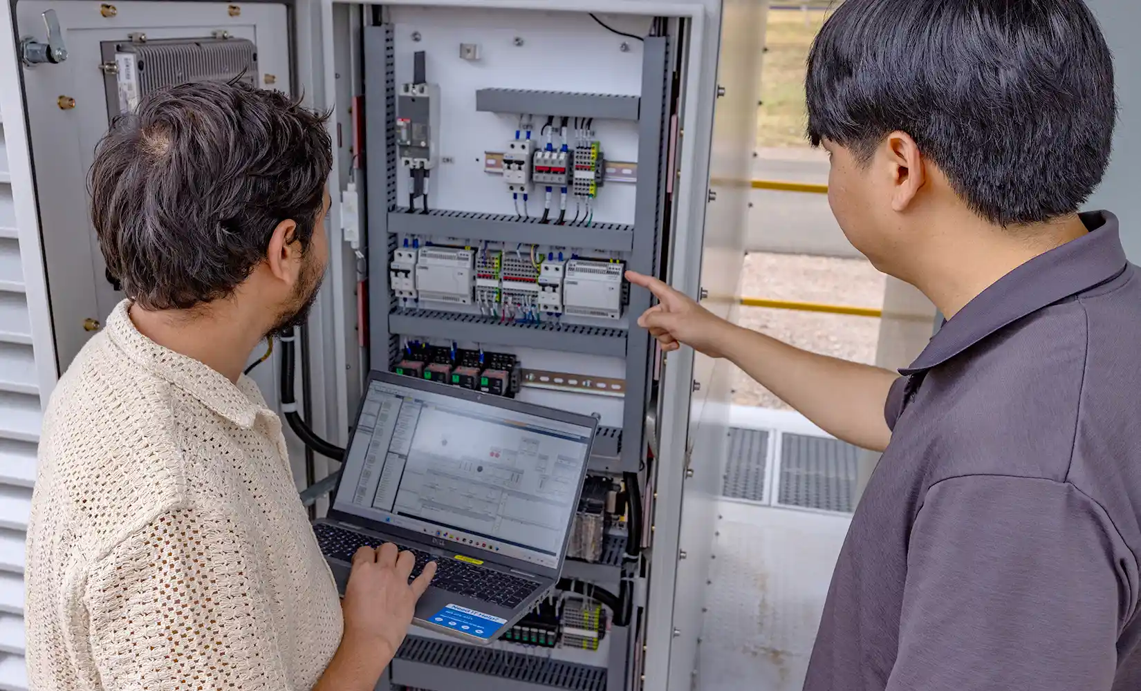 Two researchers examine electronic device and analyze results on computer.