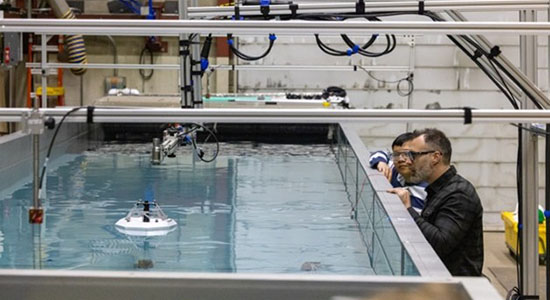 Two researchers monitor device in wave tank