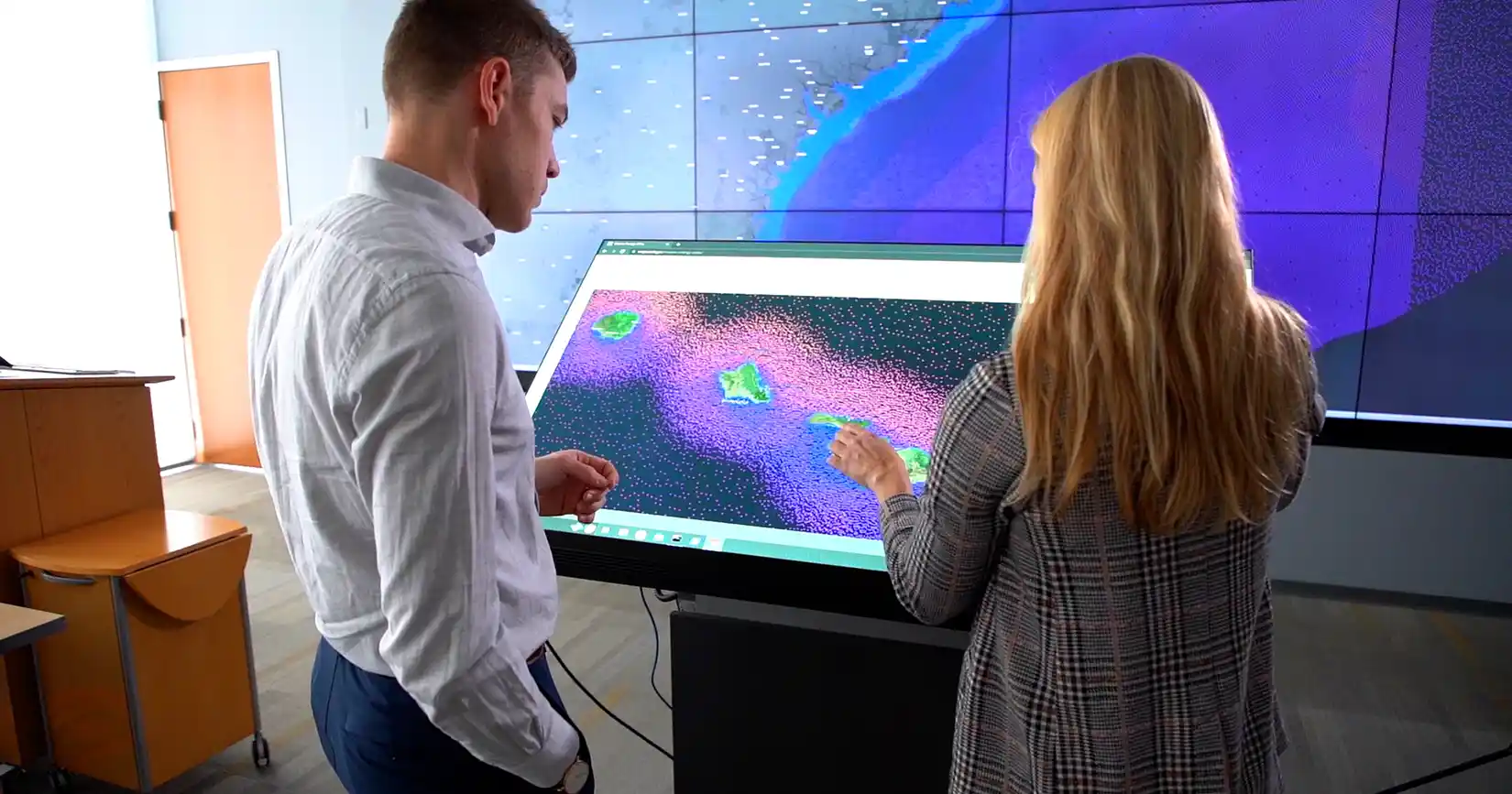 Two researchers look at the Marine Energy Atlas on a large interactive computer screen.