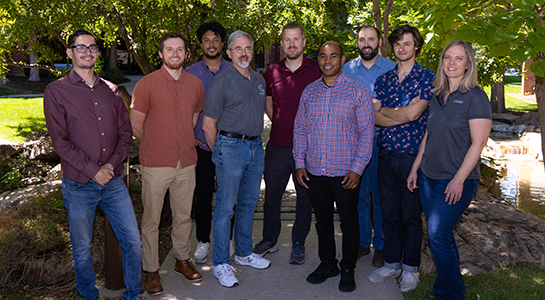 Nine people stand in front of a tree and pose for a photo.