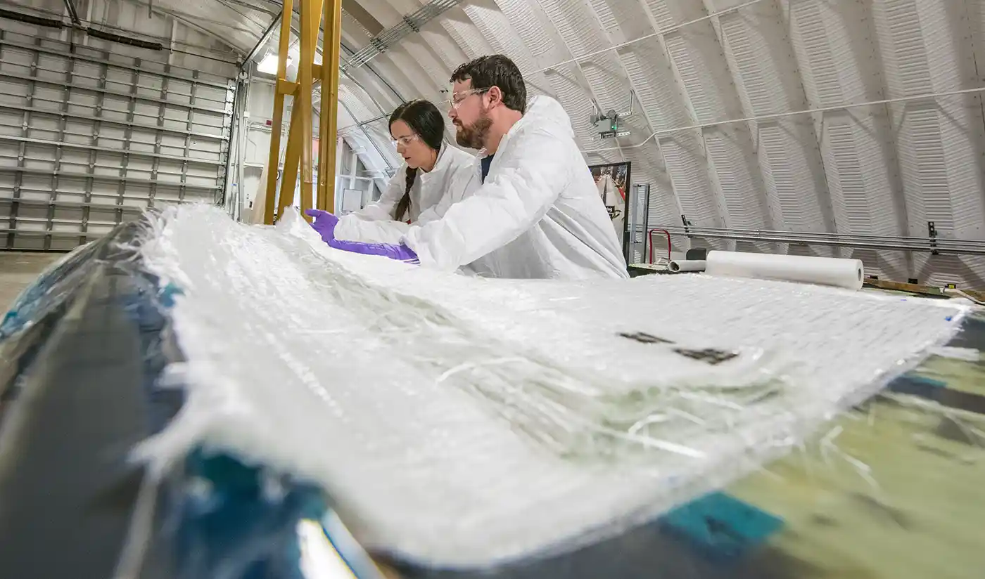 Two researchers examine wind turbine blade inside a lab.